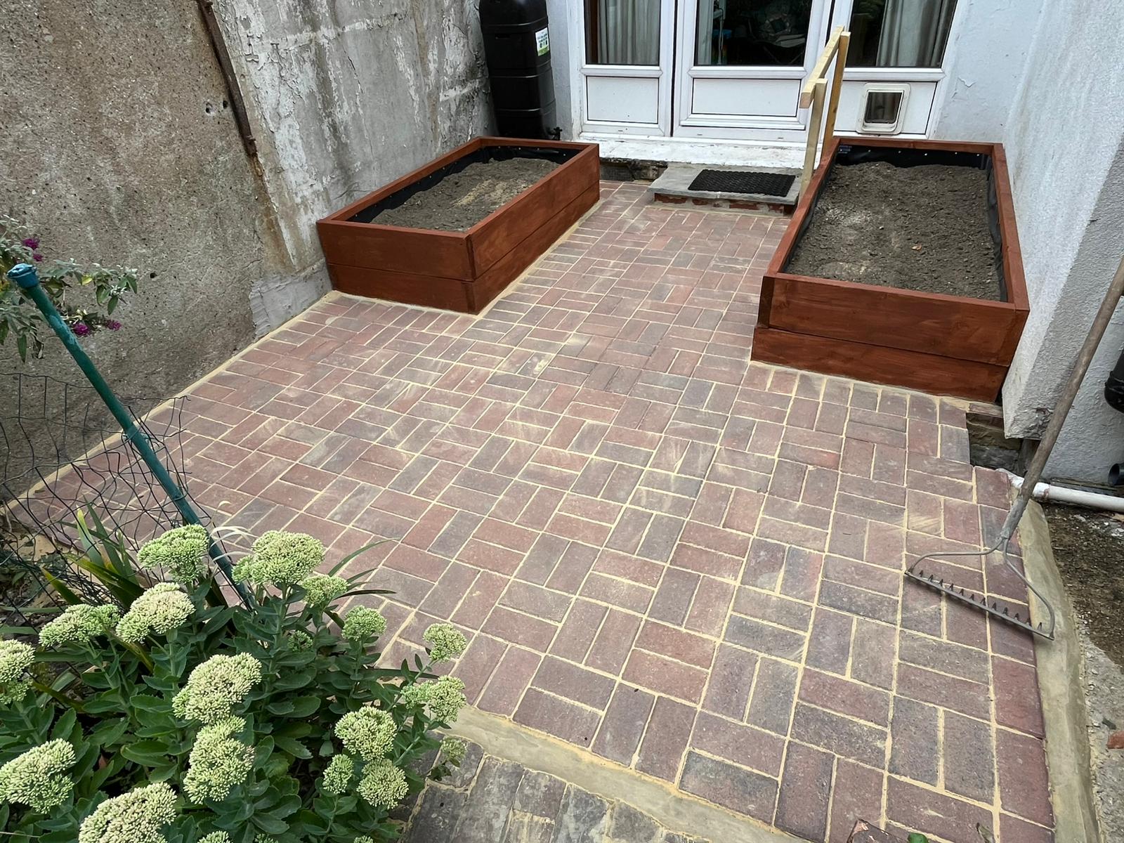 Brick paver courtyard with two timber planters by a back door.