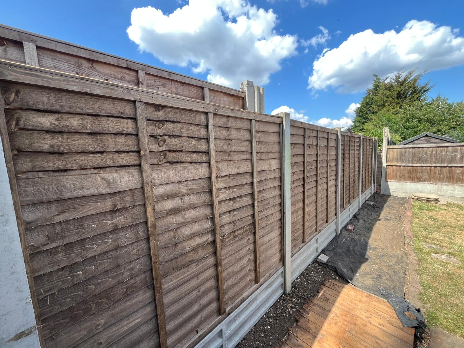 Long run of overlapping timber fence panels on concrete posts.
