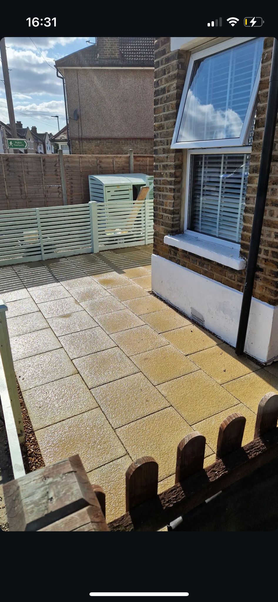 Buff coloured patio slabs in a small front courtyard with pale screening fence.