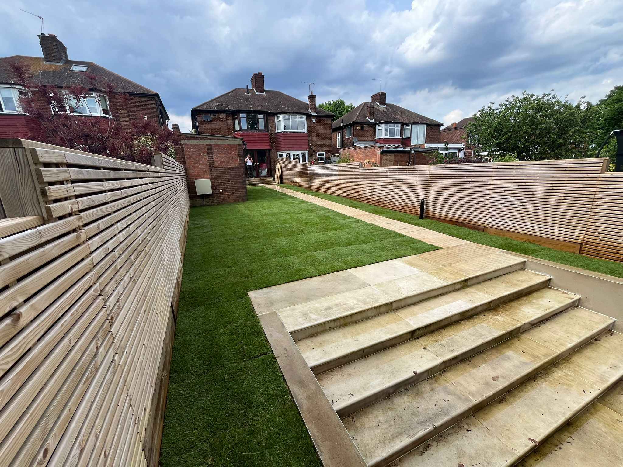 Long garden with fresh turf, wide steps and slatted timber fencing both sides.